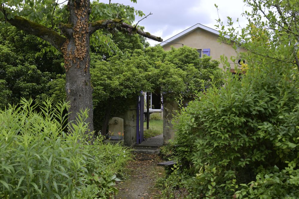 La façade de la maison aux volets lavande, vue du jardin sous les arbres